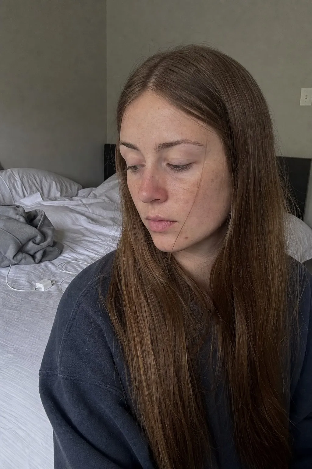A woman sitting on a bed before and after curtain bangs - before