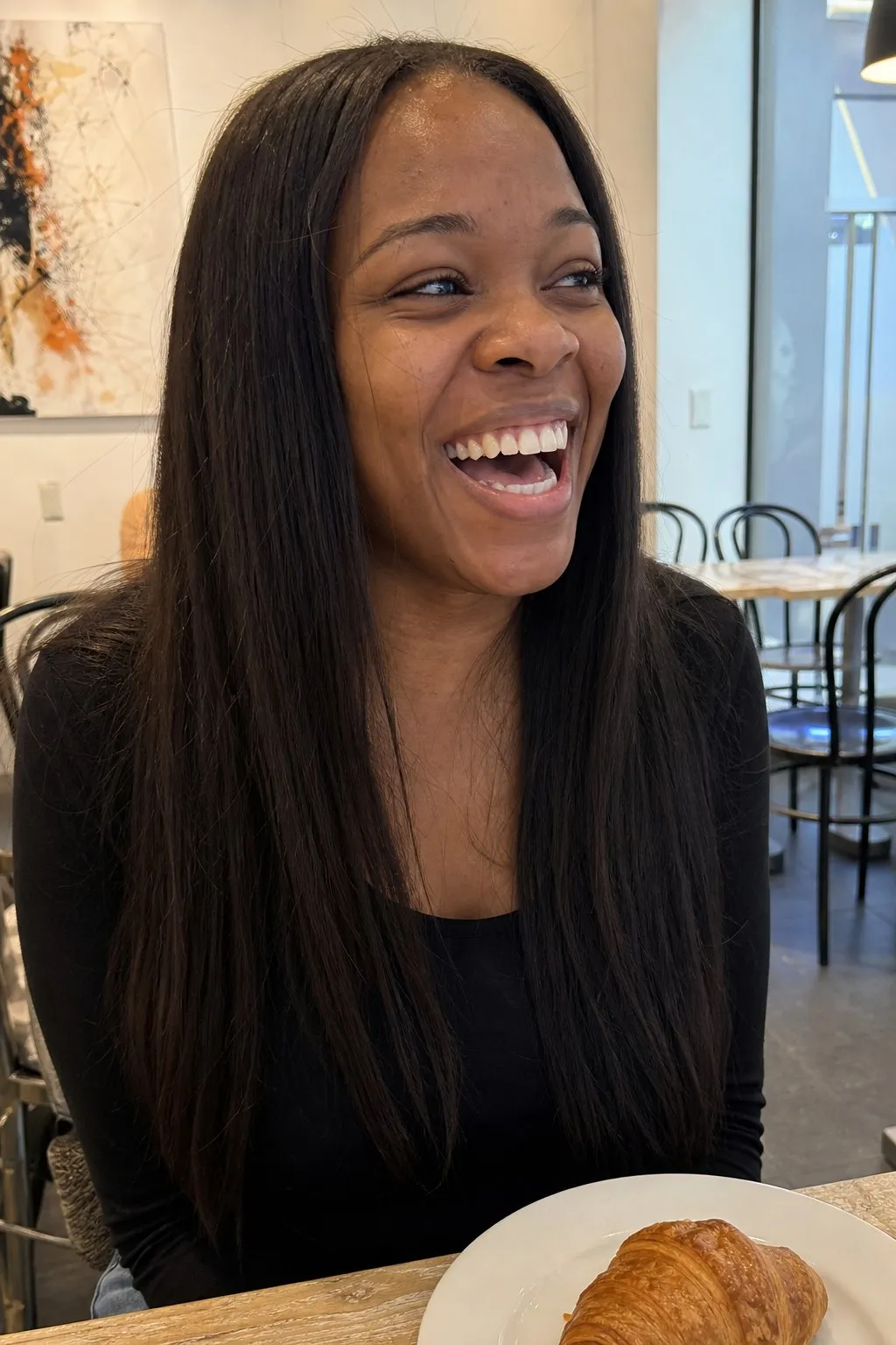 A woman laughing at a cafe table before and after face-framing layers with curtain bangs - before