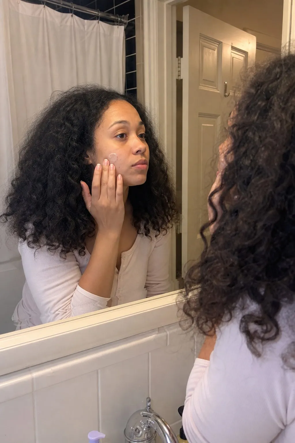 A woman in a bathroom mirror before and after layered curls - before